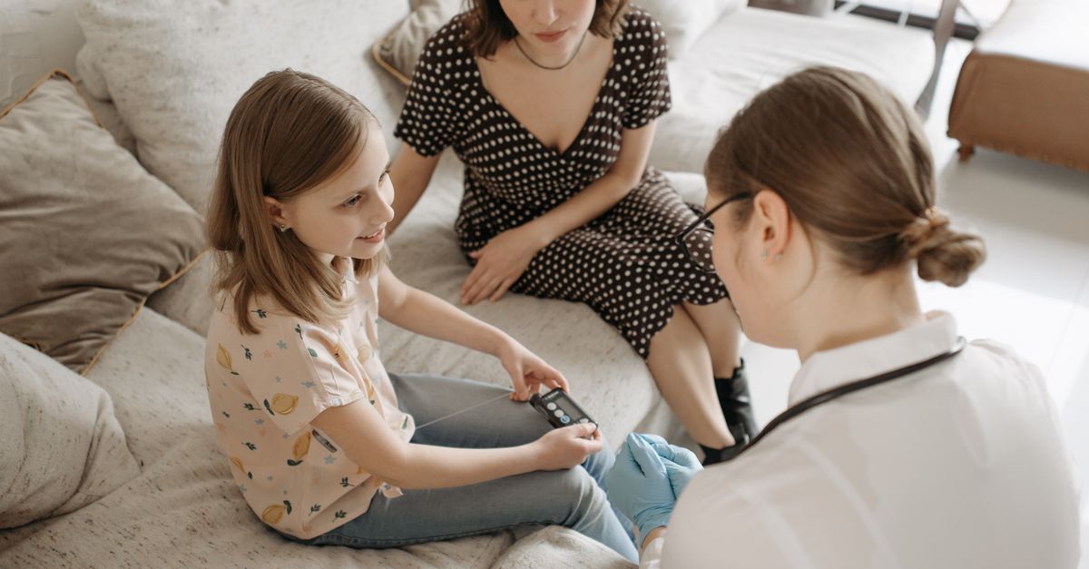 A healthcare provider assists a child with a diabetes check-up at home.